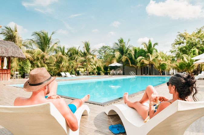 Eine Frau und ein Mann liegen auf weißen Liegen am Pool und trinken jeweils ein Getränk