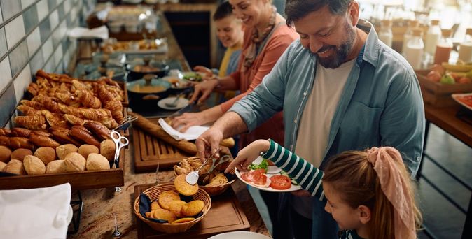 Eine Familie bedient sich lachend an einem Frühstücksbuffet