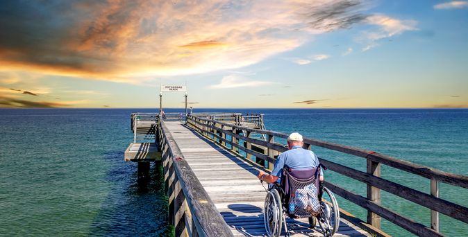 Mann im Rollstuhl auf einer Seebrücke am Meer