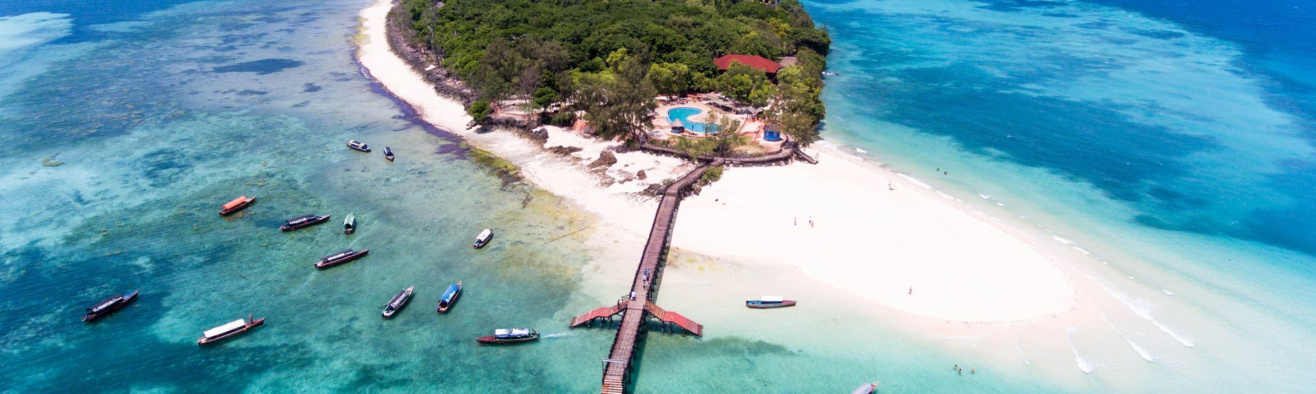 Eine kleine Insel mit Steg ins Meer, um die Insel herum schwimmen viele Boote
