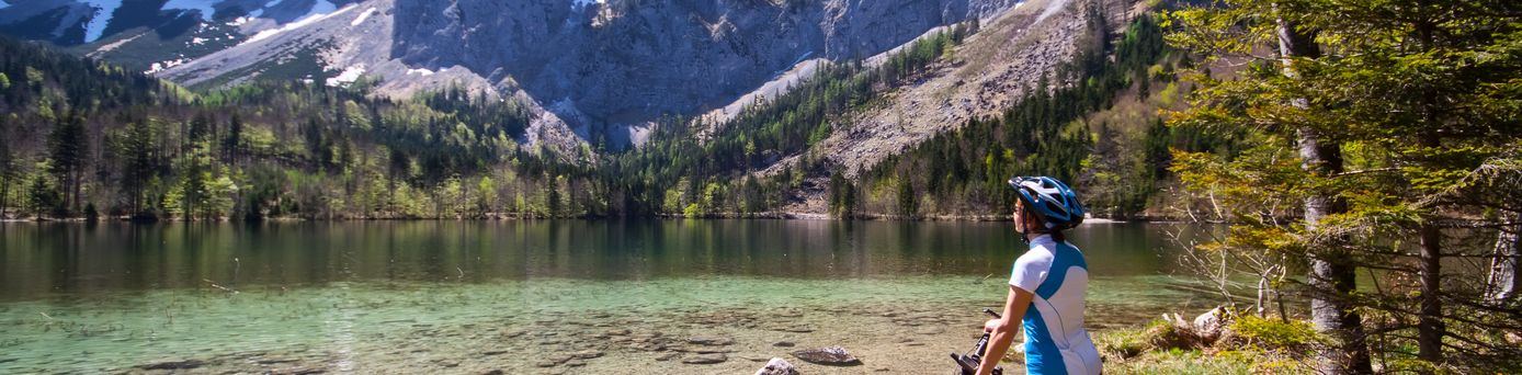 Eine Frau bestaunt auf dem Fahrrad Berge und einen See