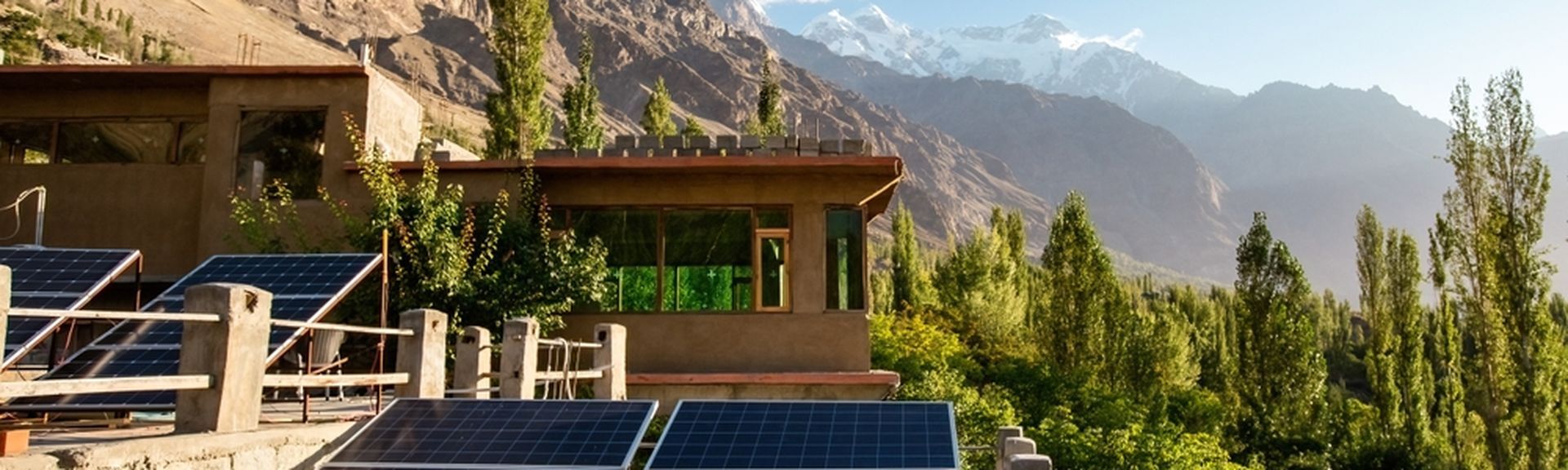 Eine Naturlandschaft mit Bergen und Bäumen, im Vordergrund ein Haus mit mehreren Solarplatten
