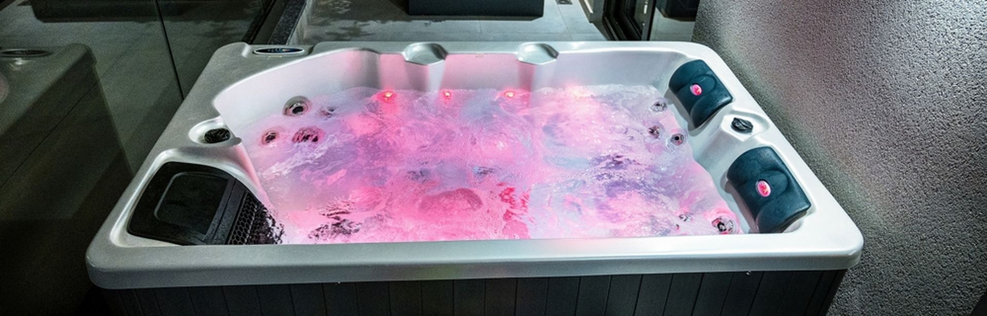 Whirlpool mit roter Beleuchtung im Wasser vor dem ein Tablet mit Obst und ein Getränk auf einem kleinen Tisch steht