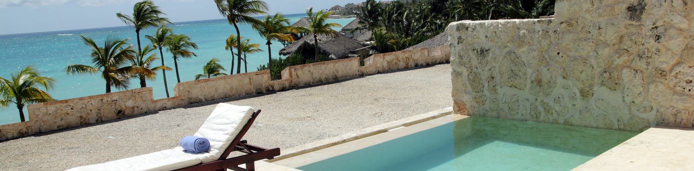 Eine höher gelegene Terrasse mit einem kleinen privaten Pool, einer Liege und Blick auf das Meer und Palmen