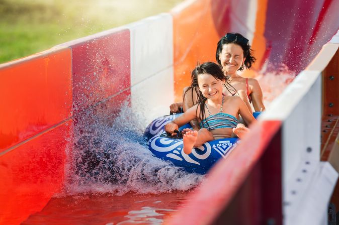 Eine Frau und ein Kind rutschen auf einem Reifen eine rote Wasserrutsche