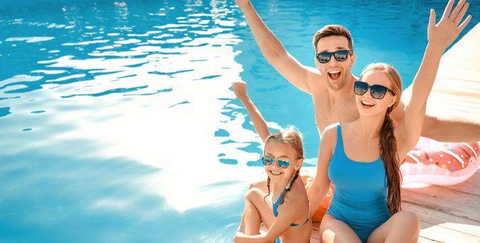 Eine Familie sitzt auf einem Steg und hält lächelnd die Arme in die Luft