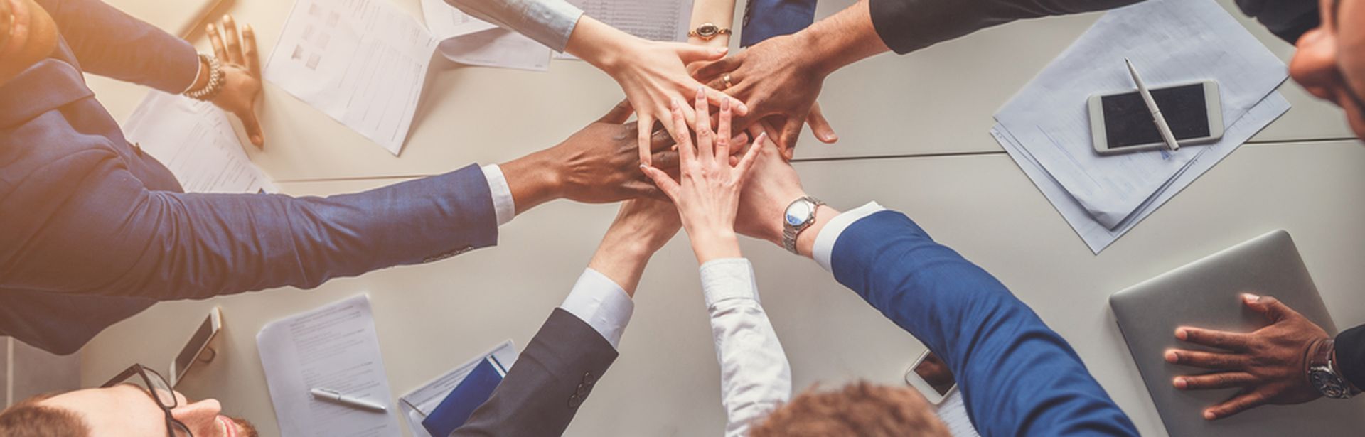 Das Bild zeigt eine Gruppe von Menschen, die jeweils eine Hand in die Mitte strecken