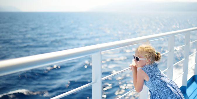Mädchen im blauen Kleid lehnt sich auf die Reling eines Schiffes und schaut auf das ruhige Meer