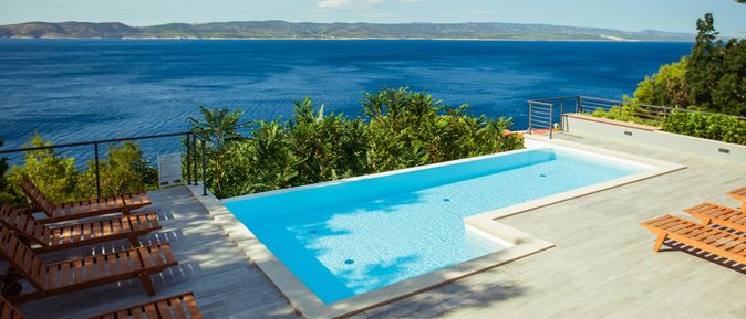 Ein Privatpool über dem Meer, um ihn herum einige Holzliegen und Bäume