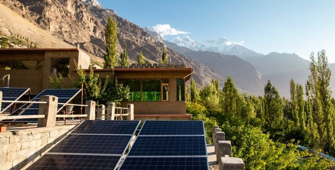 Eine Naturlandschaft mit Bergen und Bäumen, im Vordergrund ein Haus mit mehreren Solarplatten