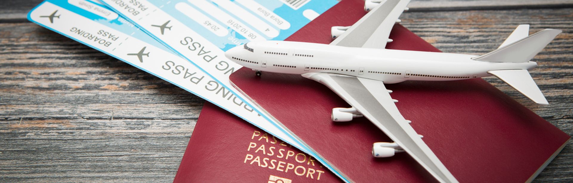 Zwei rote Reisepässe und zwei Flugtickets liegen auf einem Holztisch. Darauf liegt ein Miniaturflugzeug