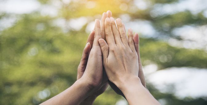 Ein Kreis aus Personen, wo jeder eine Hand in der Mitte in die Höhe zusammenhält. Zu sehen sind nur die Hände