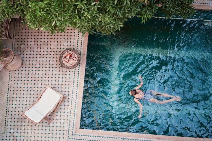 Frau schwimmt in einem Pool; Neben dem Pool, auf der Terrasse steht eine Liege