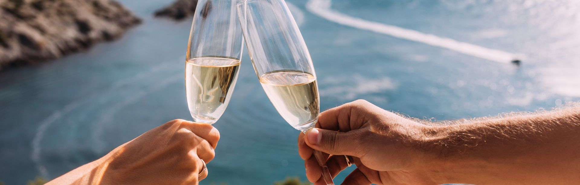 Zwei Hände stoßen mit Sektgläsern am Meer an