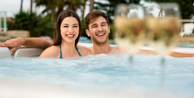 Ein Paar sitzt im Whirlpool, während unscharf im Vordergrund zwei gefüllte Gläser zu sehen sind