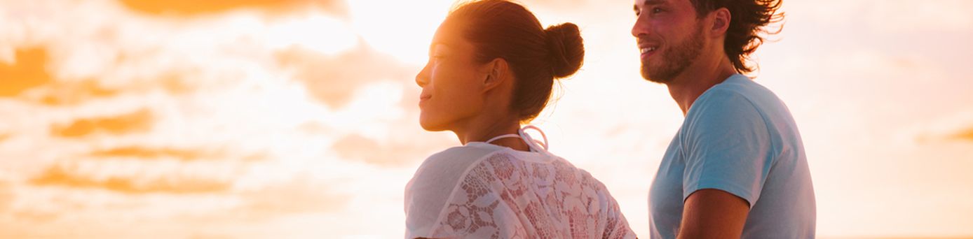 Eine Frau und ein Mann stehen bei Sonnenuntergang an der Reling eines Kreuzfahrtschiffes
