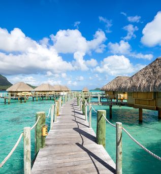 Ein Steg führt zu einer Reihe vom Wasserbungalows durch türkisblaues Wasser