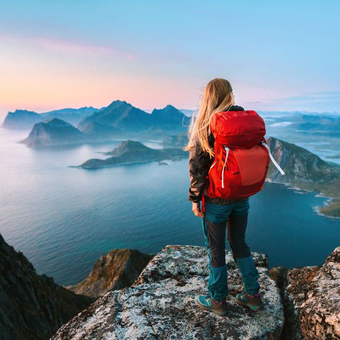 Alleinreisende Frau mit Rucksack schaut von einem Berg auf Wasser 