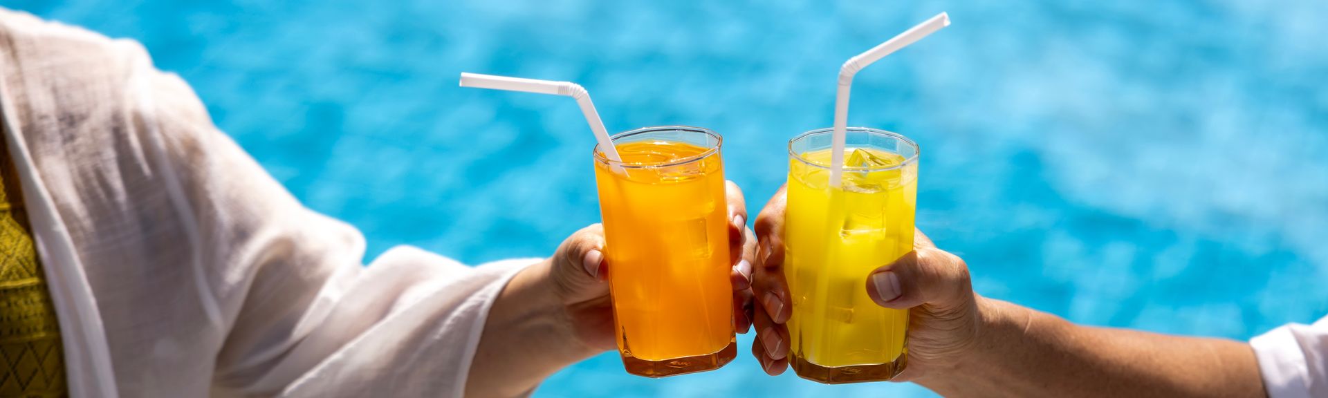 Zwei Hände stoßen mit Gläsern über einem Pool an