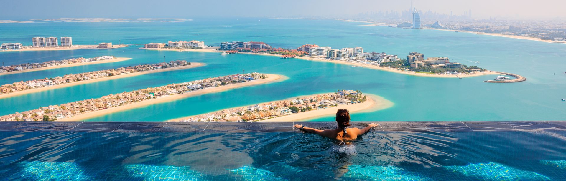 Frau am Rand eines Infinity-Pools, mit Blick auf bebauten Inseln im Meer