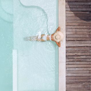 Eine Frau mit weißem Sonnenhut lehnt am Rand eines eleganten Pools