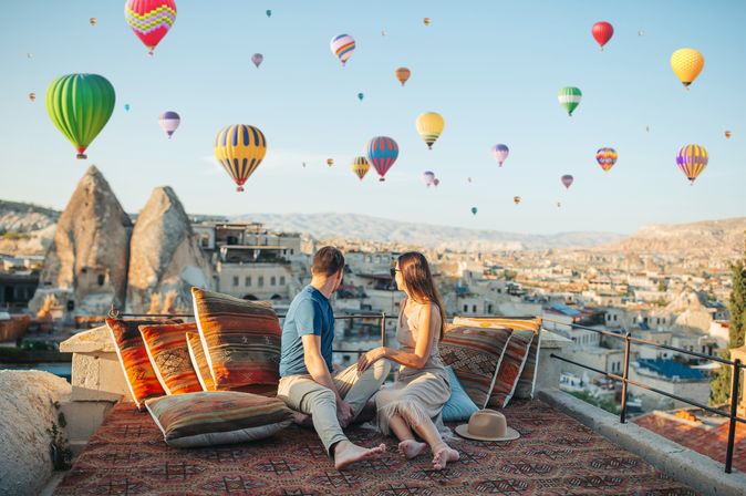 Fröhliches junges Paar beim Sonnenaufgang mit Heißluftballons in Kappadokien