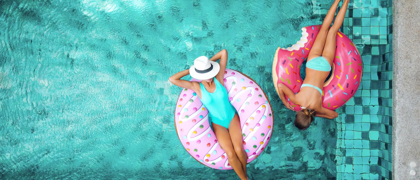 Zwei Frauen liegen in Donut Pool Floaties im Pool