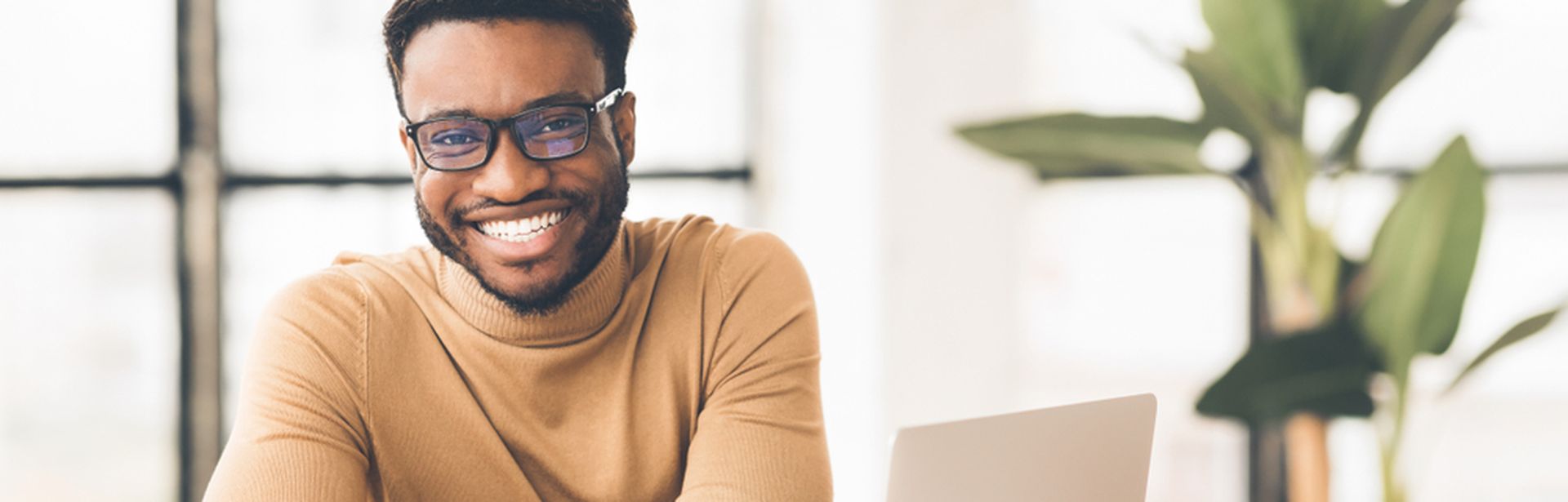 Ein Mann sitzt an einem Schreibtisch und lehnt mit dem Armen auf dem Tisch. Auf dem Schreibtisch befinden sich ein Laptop und ein paar Zettel