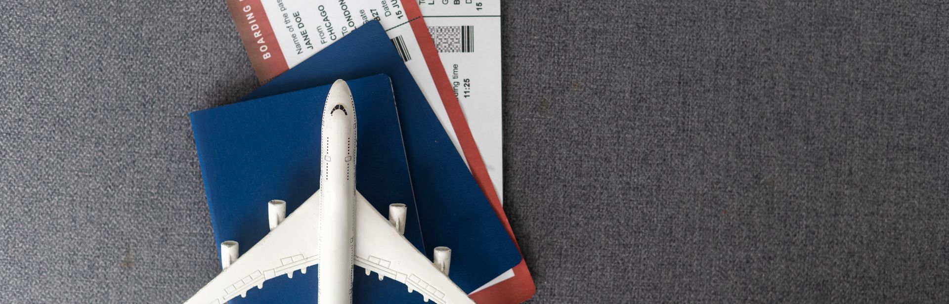 Ein Miniaturflugzeug liegt auf einem Reisepass in dem sich zwei Flugtickets befinden