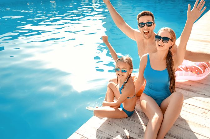 Eine Familie sitzt auf einem Steg und hält lächelnd die Arme in die Luft