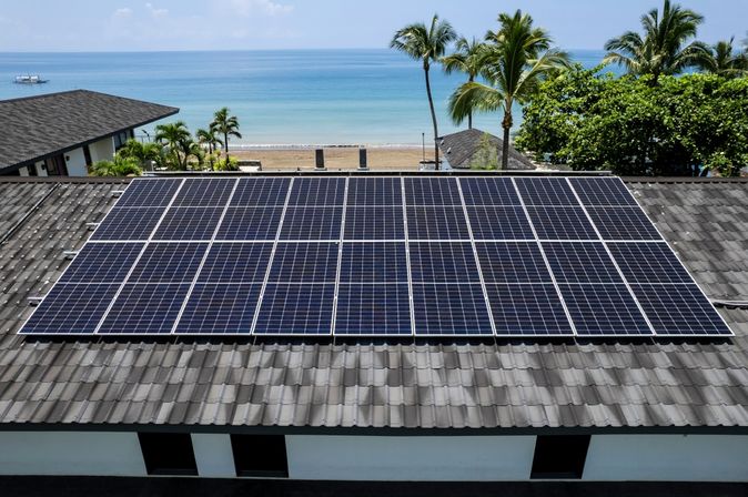 Ein Dach mit Solarplatten, im Hintergrund ein Strand und das Meer