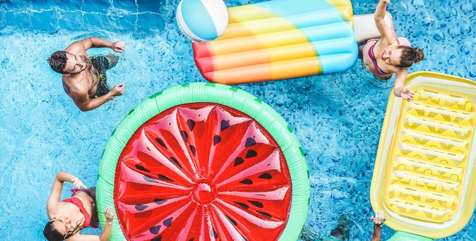 Ein Pool von oben, mehrere Personen und Pool Floaties in Frucht Formen