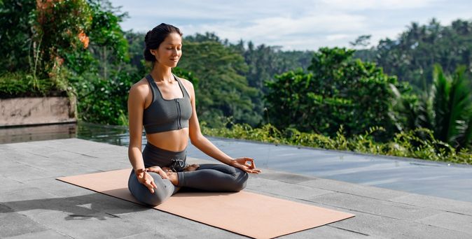 Eine Frau meditiert im Schneidersitz auf einer Yogamatte