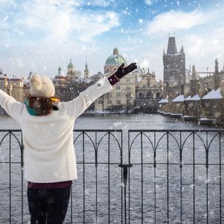 Eine Frau steht vor einem Zaun an einem Fluss, der durch eine Stadt fließt, während es schneit