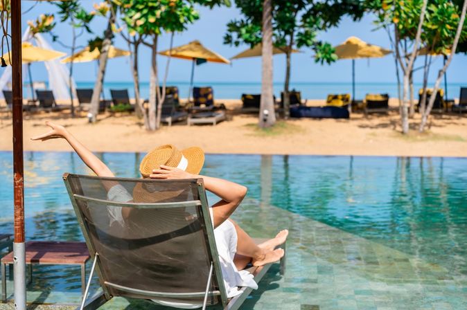 Frau sitzt auf einer Liege am Pool mit Strandzugang