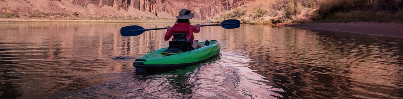 Eine Person sitzt in einem Grünen Kanu und schaut auf einen pinken Sonnenauf/untergang
