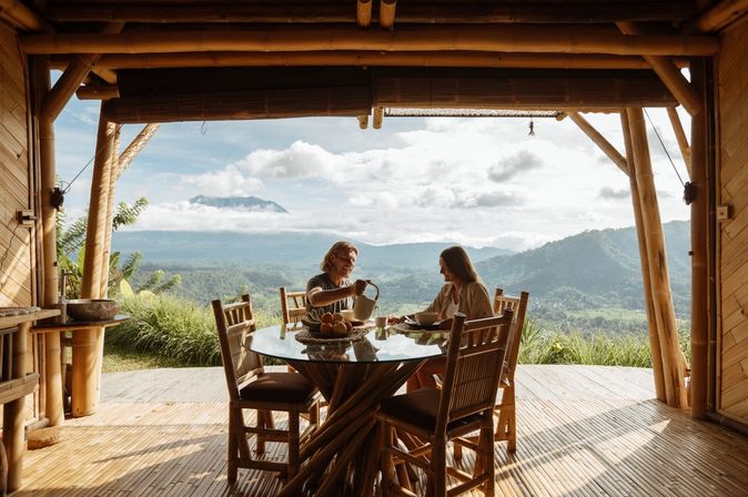 Auf einer Terrasse mit beeindruckendem Ausblick auf eine grüne Landschaft sitzen zwei Personen an einem Tisch 