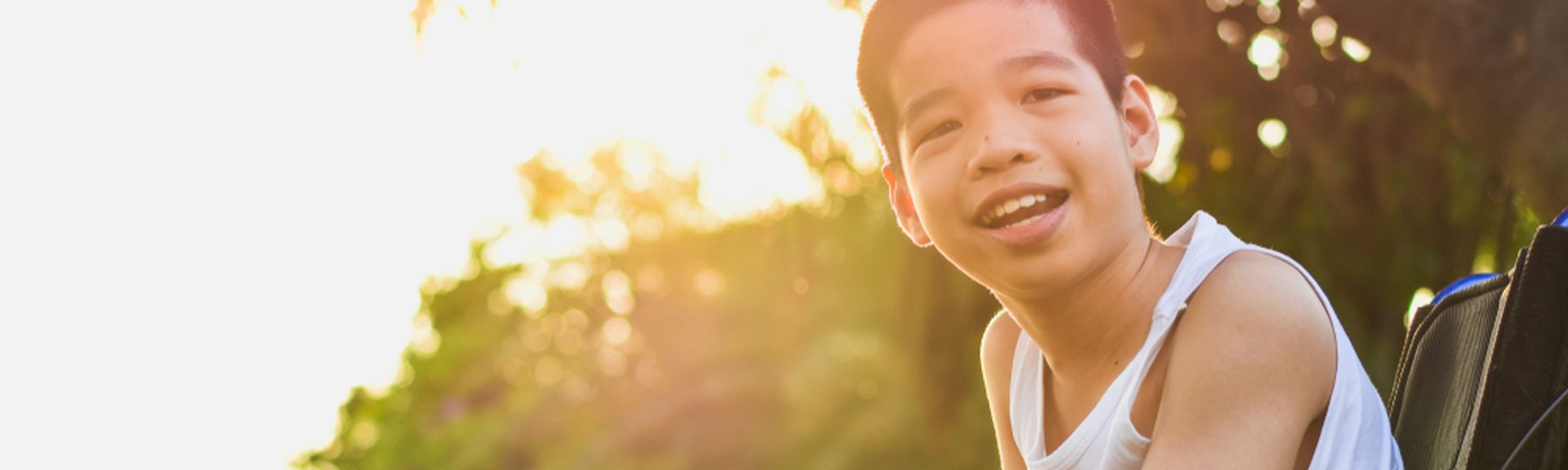 Junge im Rollstuhl in der Natur lächelt in die Kamera