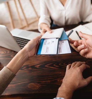 Eine Frau sitzt am Schreibtisch und übergibt zwei Personen Ihre Flugtickets