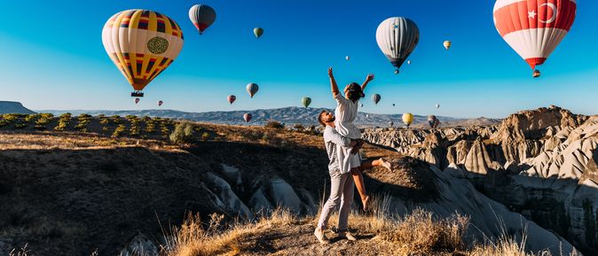 Ein Mann trägt eine Frau im Arm, um Sie herum schweben Heißluftballons durch die Luft