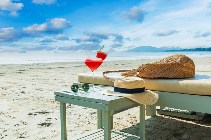 Eine Liege und ein Tisch mit einem Sonnenhut und einem Getränk am Strand