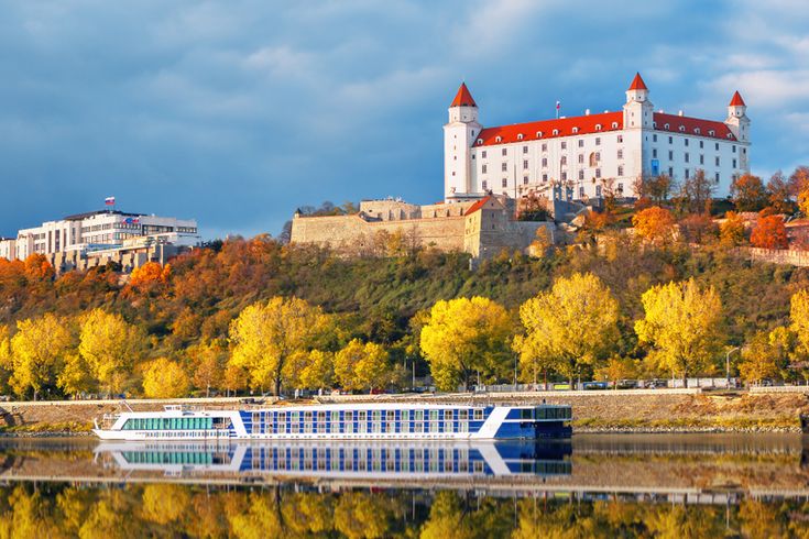 Flusskreuzfahrtschiff fährt an einer herbstlichen Landschaft mit einem weißen Schloss vorbei