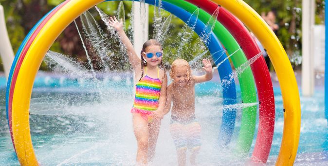 Zwei Kinder laufen durch bunte Bögen aus denen Wasser auf sie gespritzt wird