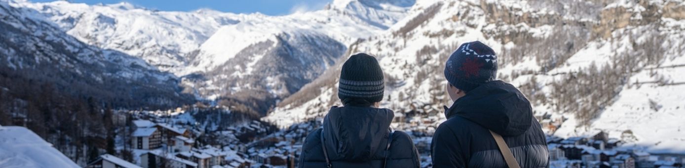 Zwei Personen stehen erhöht und schauen auf ein verschneites Dorf in den Bergen