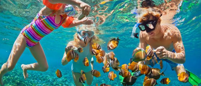 Drei Kinder schauen sich mit Taucherbrillen bunte Fische unter Wasser an