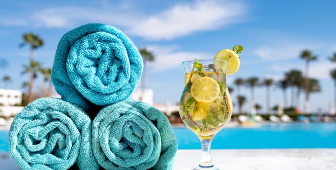 Handtücher und ein Getränk stehen am Pool mit Palmen im Hintergrund