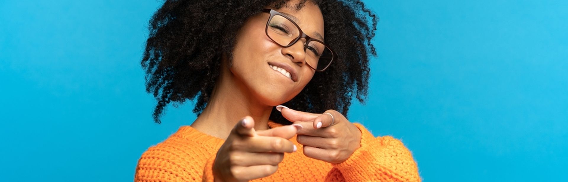 Frau zeigt in die Kamera vor blauem Hintergrund