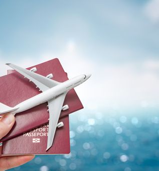 Eine Hand hält vor einem blauen Hintergrund zwei Reisepässe und ein Miniaturflugzeug hoch