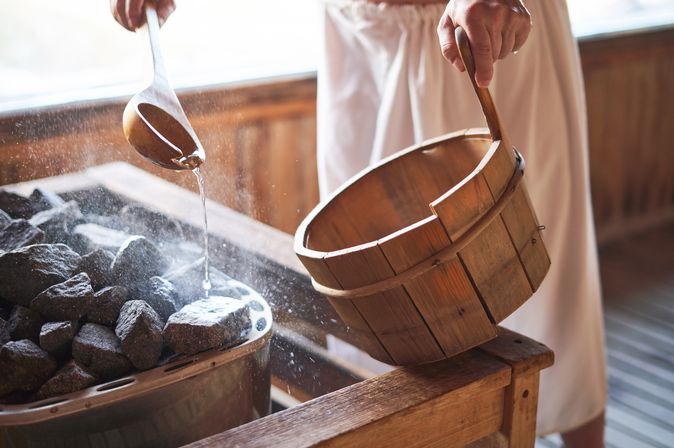 Ein Mann gießt Wasser auf heiße Steine in einer Sauna