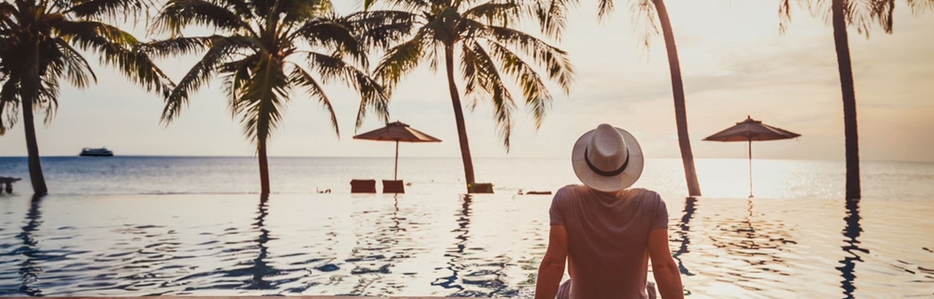 Mann sitzt auf einem Steg am Wasser und schaut in die Sonne